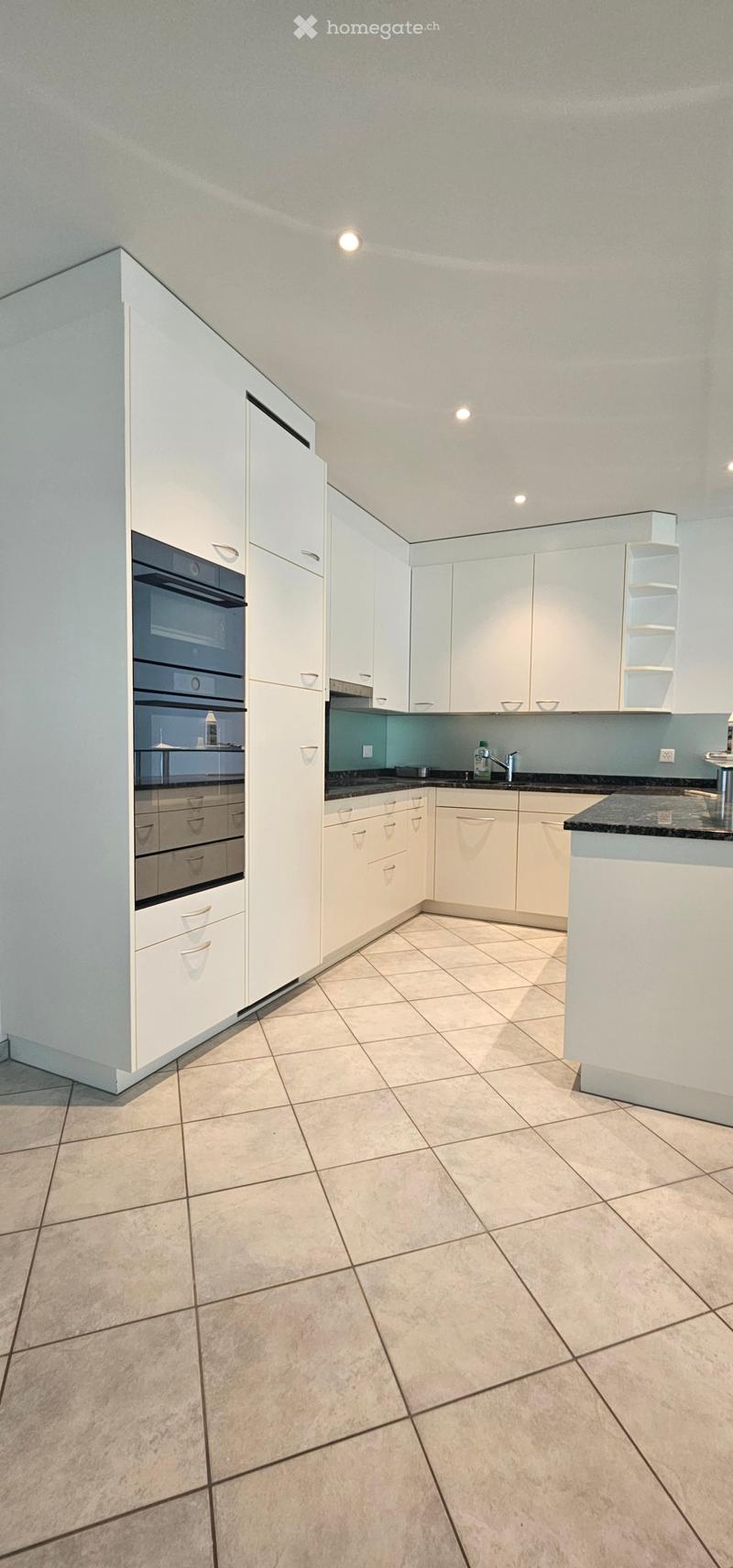 Empty kitchen with white cabinets, tiled floor, and black countertops. No appliances or furniture are present.
