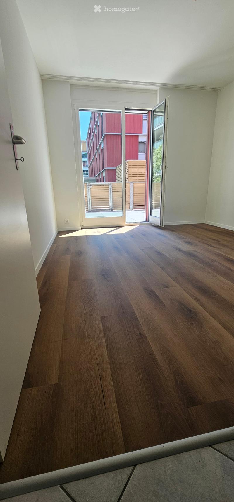 Empty room with wooden flooring, white walls, and a large sliding glass door leading to an outdoor area.
