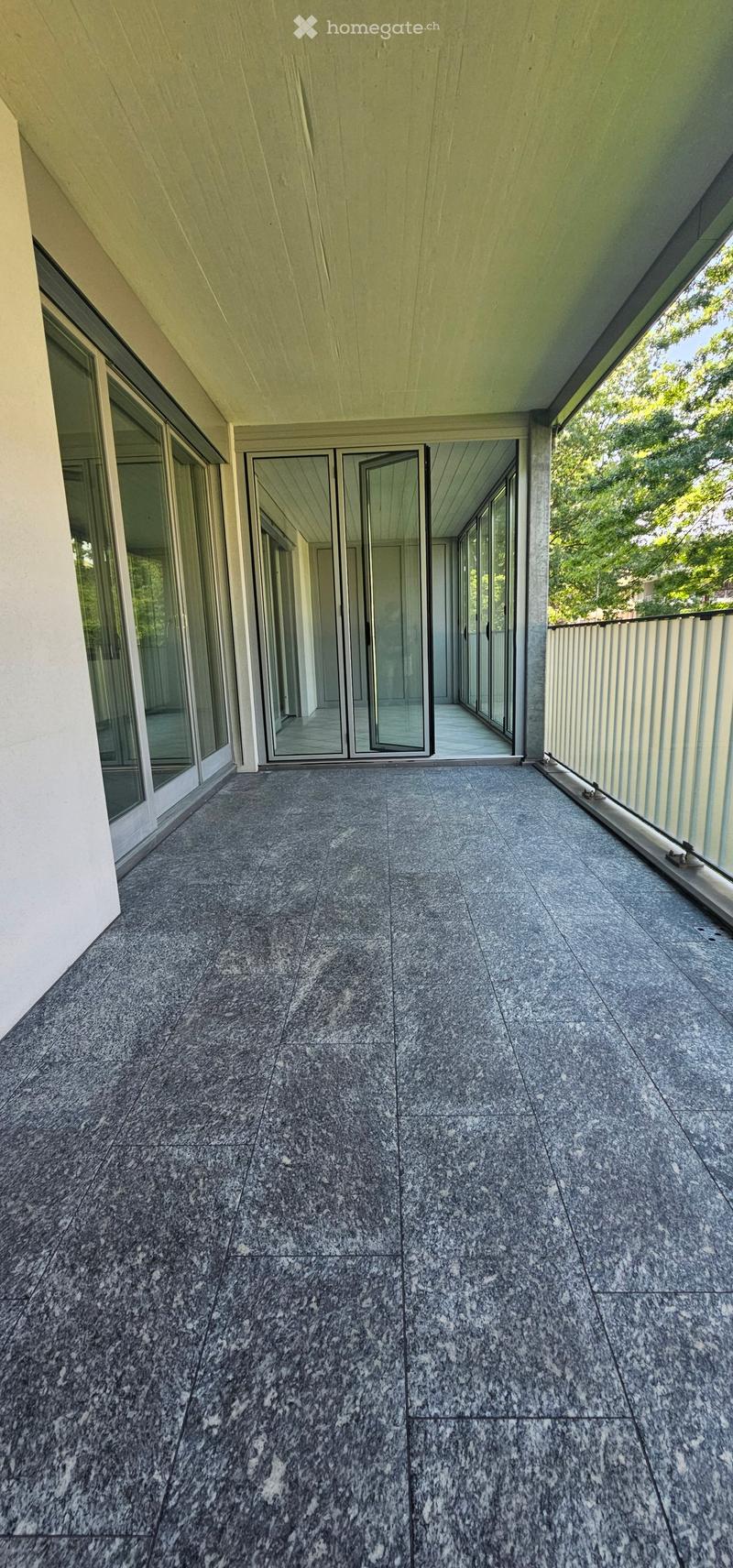 Modern balcony with large glass sliding doors, grey tiled floor, and white metal railing.