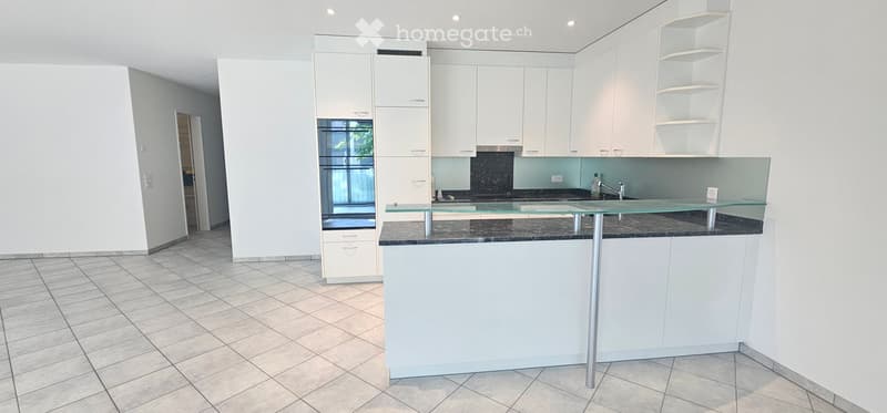 Modern kitchen with white cabinets, a central island, and a glass countertop. Features a black granite backsplash and tiled flooring.