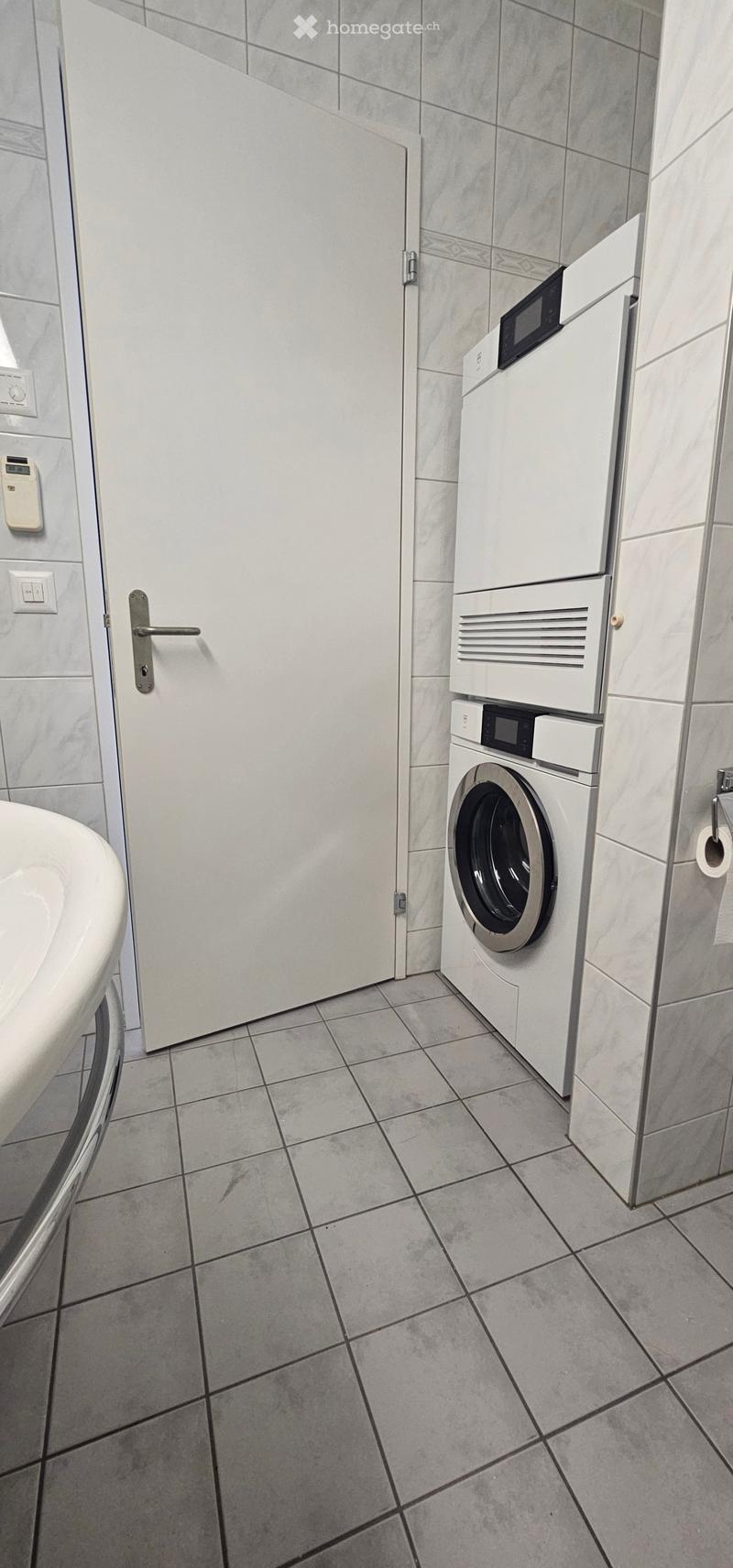 Clean bathroom with tiled walls and floor, featuring a washing machine and a closed door.