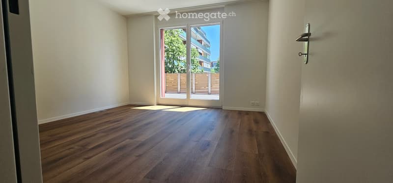 Empty room with wooden flooring, white walls, and large sliding glass doors leading to a balcony or outdoor area.