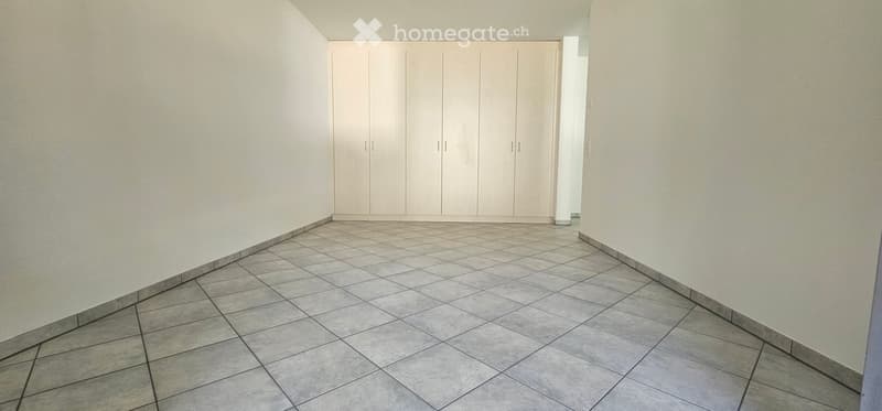 Empty room with tiled floor and white walls, featuring built-in white closet units.