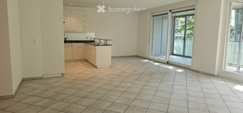 Empty room with tiled flooring, white walls, and a small kitchen area with cabinets and a countertop. Large sliding glass doors lead to a balcony.