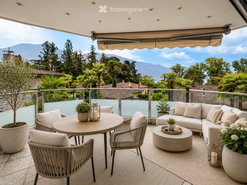 A modern outdoor terrace with a round dining table, wicker chairs, a sectional sofa, and potted plants, overlooking a scenic mountain view.