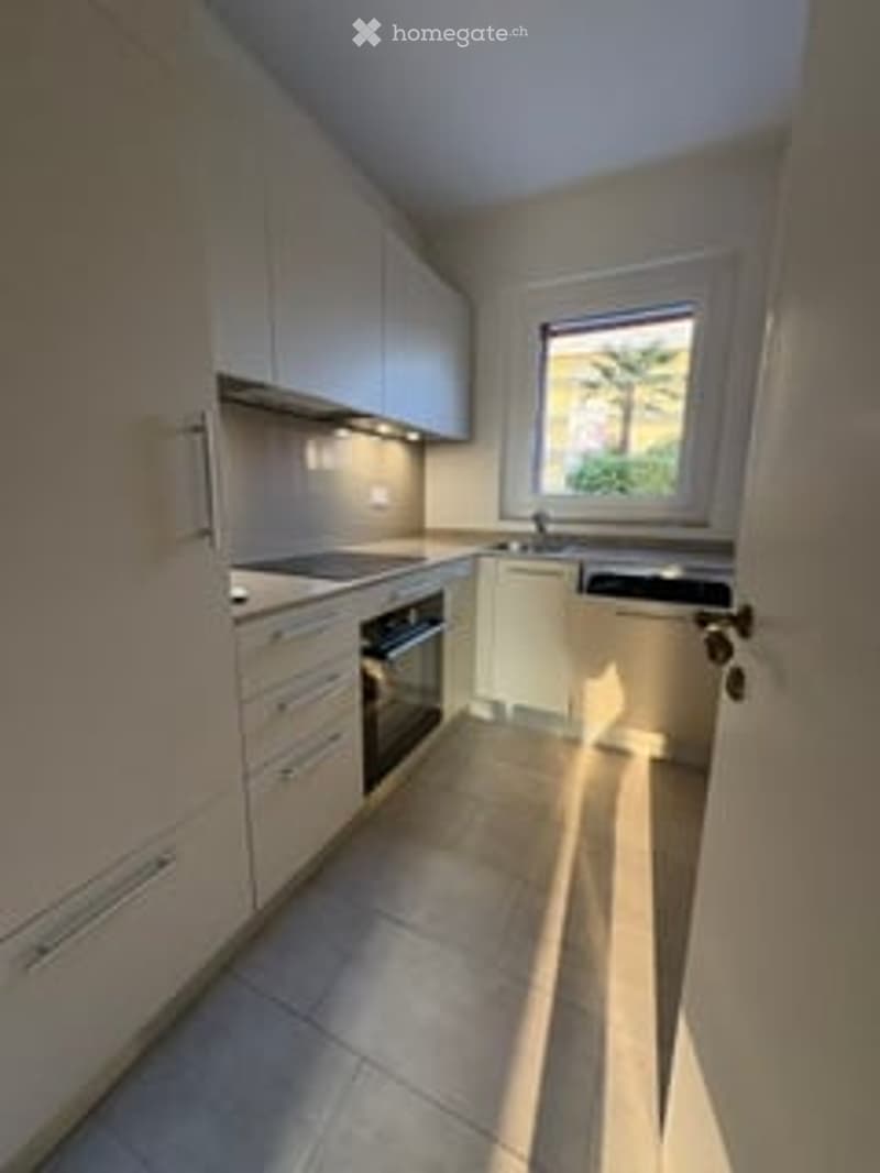 Modern kitchen with white cabinets, a stove, an oven, and a sink, featuring a large window with a view of greenery.