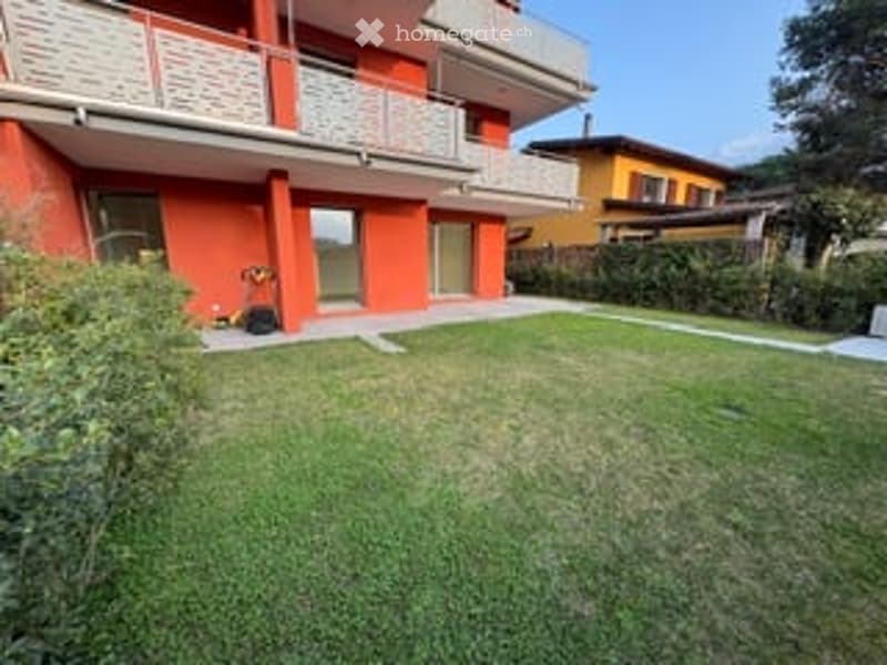 Well-maintained lawn in front of a red apartment building with balconies and large windows.