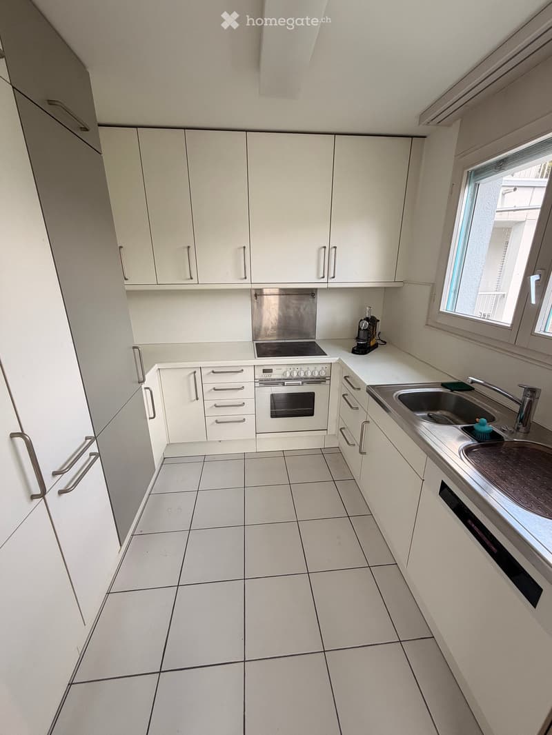 Modern kitchen with white cabinets, stainless steel appliances, tiled floor, and a window with blinds.
