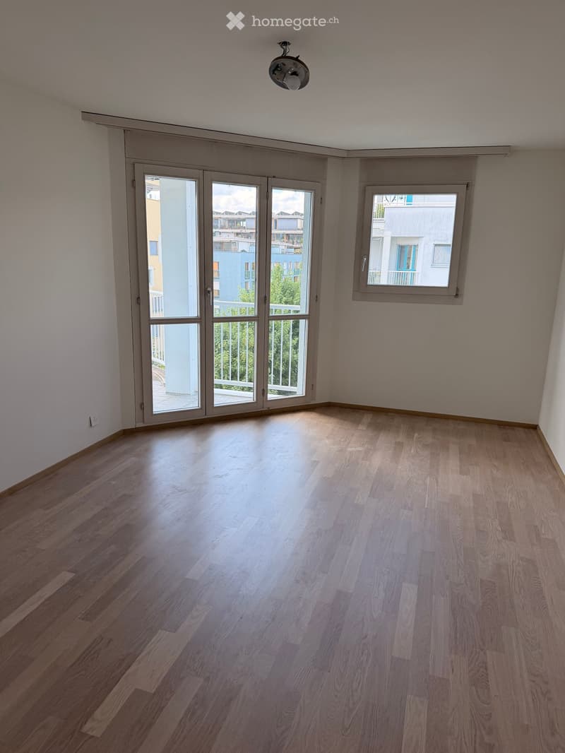 Empty room with wooden flooring, large sliding glass doors leading to a balcony, and a window on the side wall.