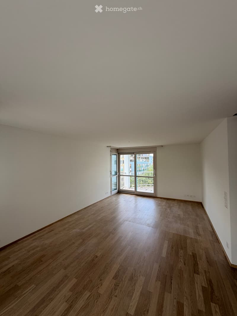 Empty room with wooden flooring and white walls, featuring a sliding glass door leading to a balcony.