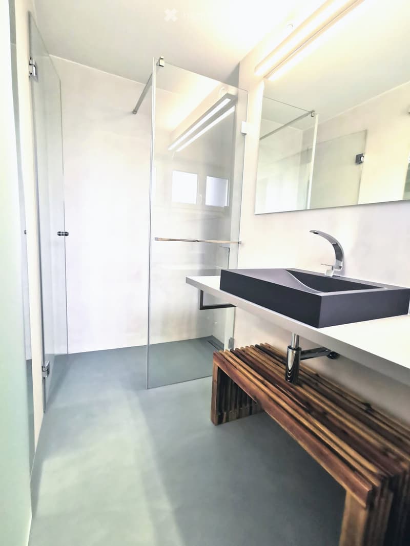 Modern bathroom with a sleek black sink, chrome faucet, large mirror, and a wooden bench under the sink.