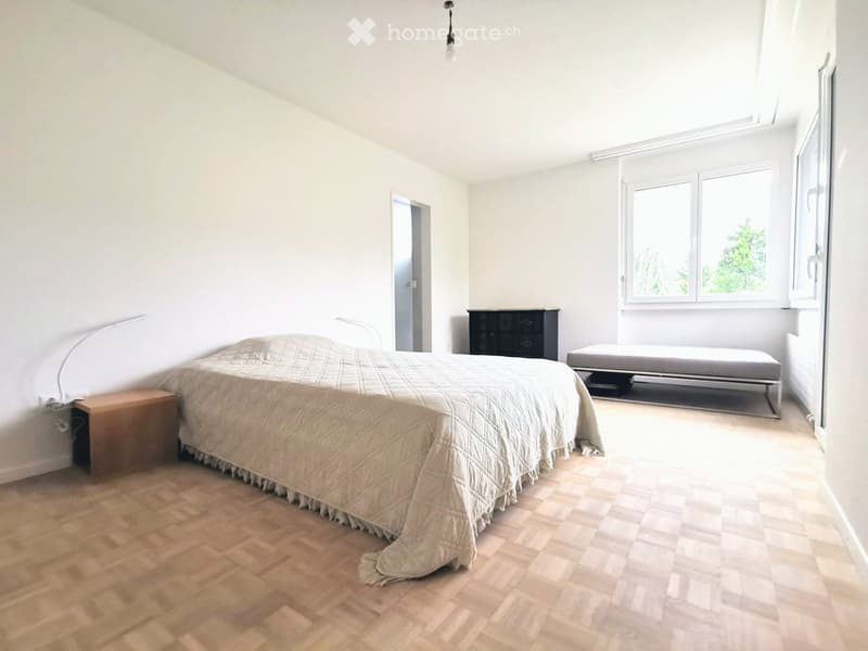Bright bedroom with wooden herringbone flooring, large window, bed with quilt, nightstand, chest of drawers, and daybed.