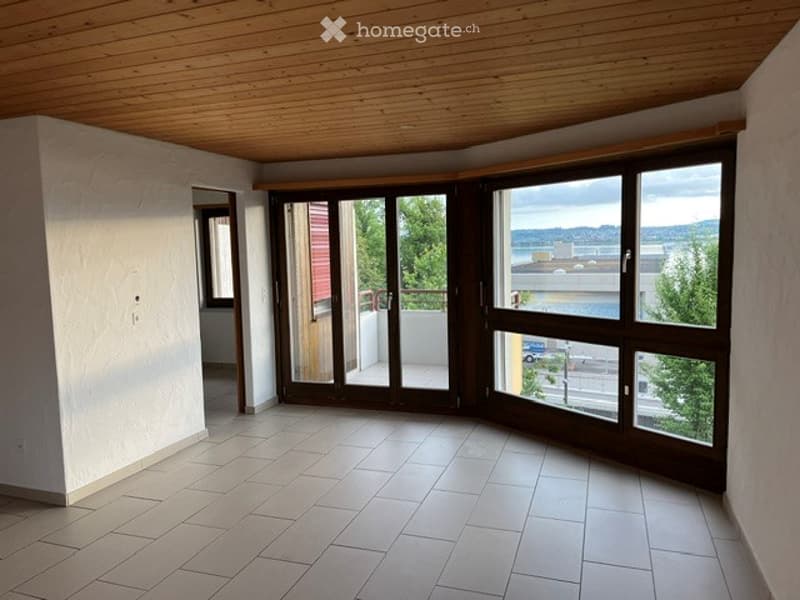 Empty room with large windows offering a scenic view, wooden ceiling, tiled floor, and sliding glass doors leading to a balcony.