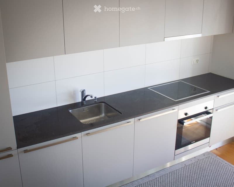 Modern kitchen with white cabinets, black countertops, stainless steel sink, induction cooktop, and built-in oven.