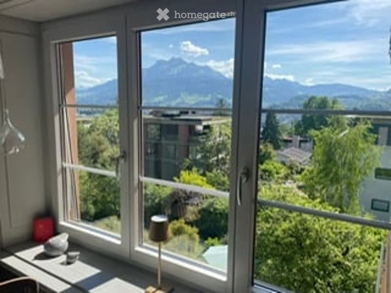 Balcony with large windows offering a scenic mountain view, featuring a small table lamp and a stool.