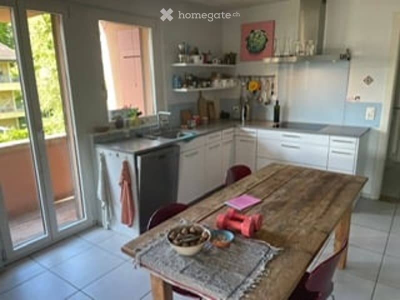Bright, modern kitchen with white cabinets, stainless steel appliances, a wooden dining table, and a view to a balcony.