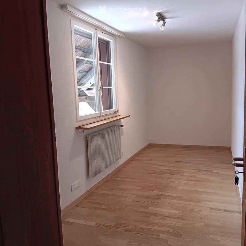 Empty room with wooden flooring, white walls, a window with a shelf, and a radiator below it.