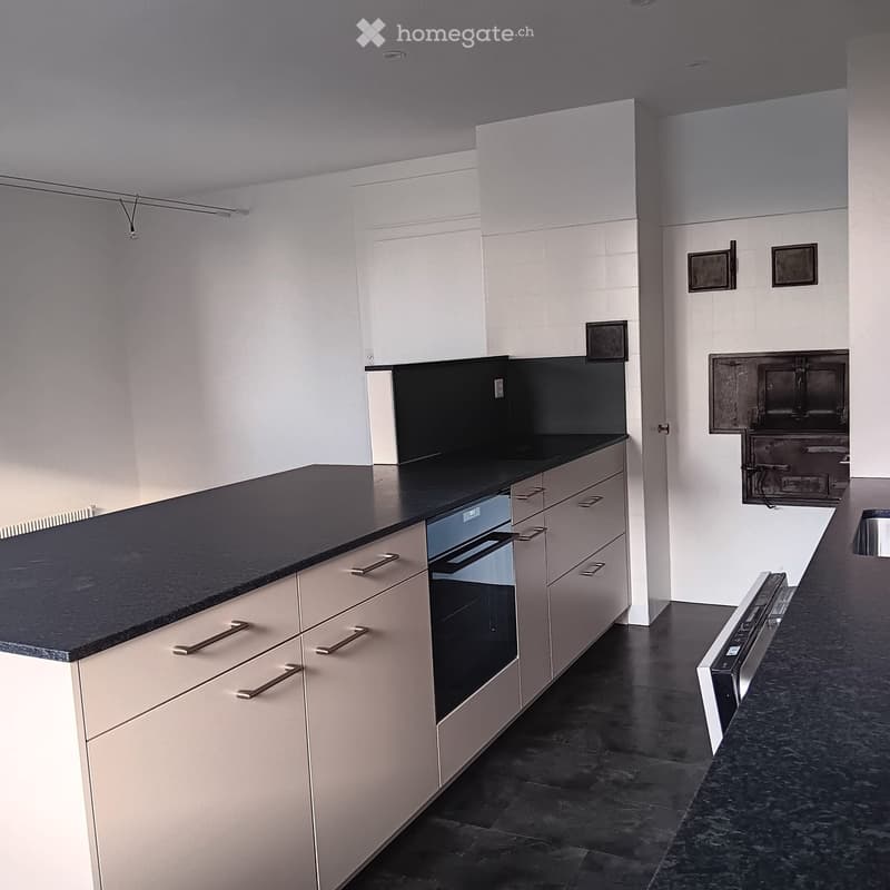 Modern kitchen with white cabinets, black countertop, and built-in oven. Dark tiled floor and sleek design.