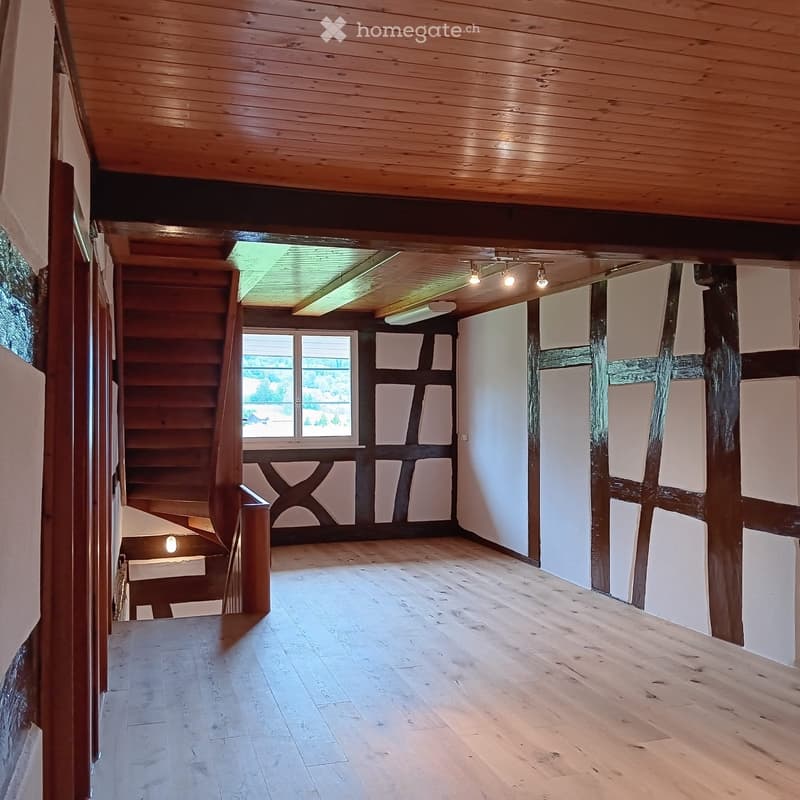 Empty room with wooden ceiling, wooden floor, staircase, and large windows with a view of greenery.