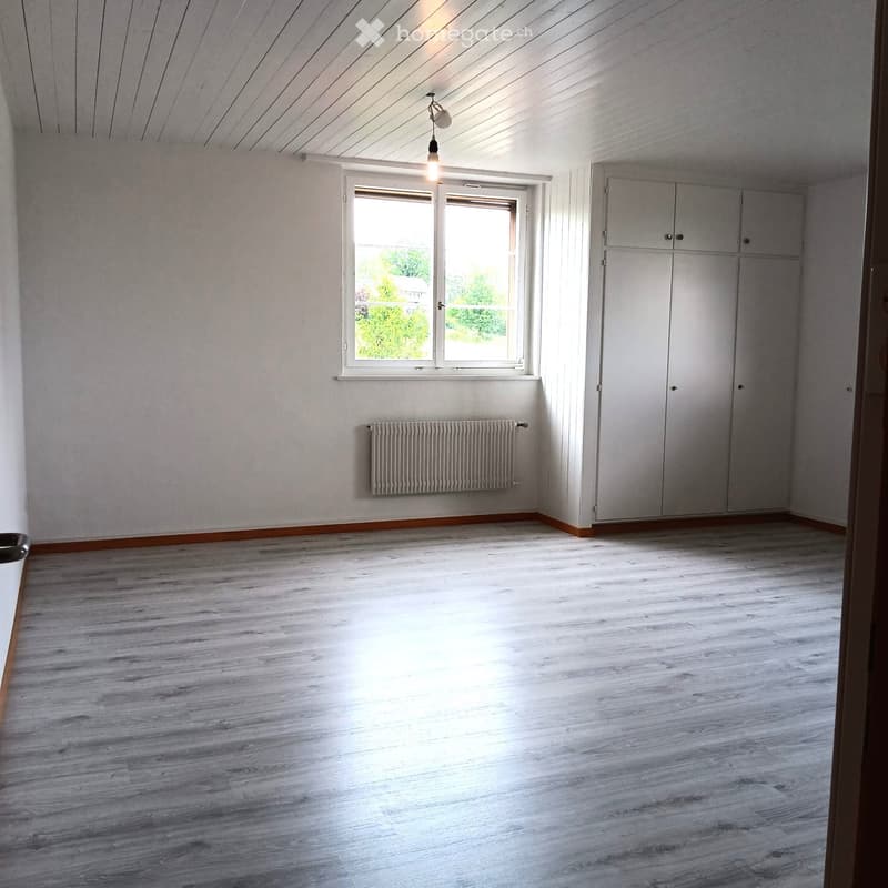 Empty room with light wooden flooring, white walls, a window with white frame, a radiator, and a built-in closet with double doors.