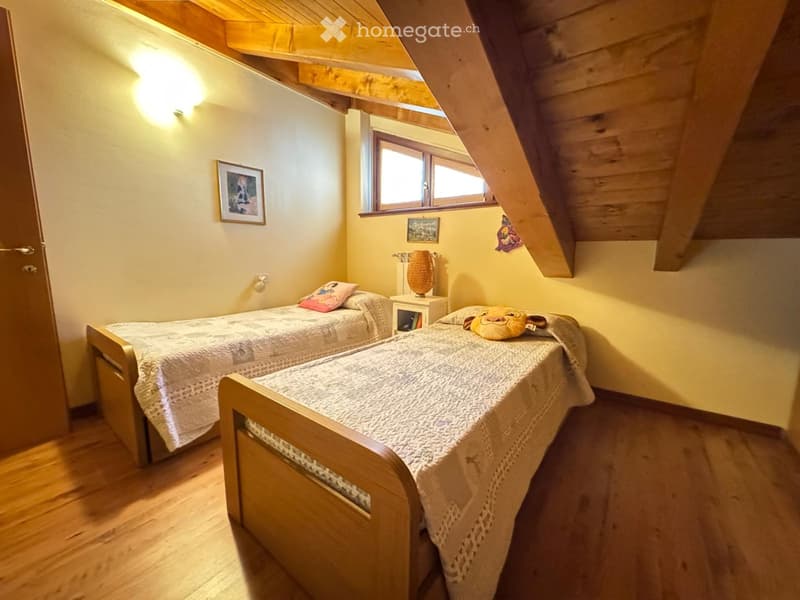 Cozy attic bedroom with two single beds, wooden floors, slanted wooden ceiling, and warm lighting.