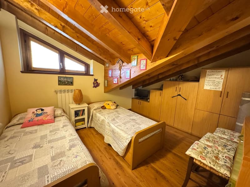 Cozy attic bedroom with wooden slanted ceilings, two single beds, nightstand, small cabinet, and a window letting in natural light.