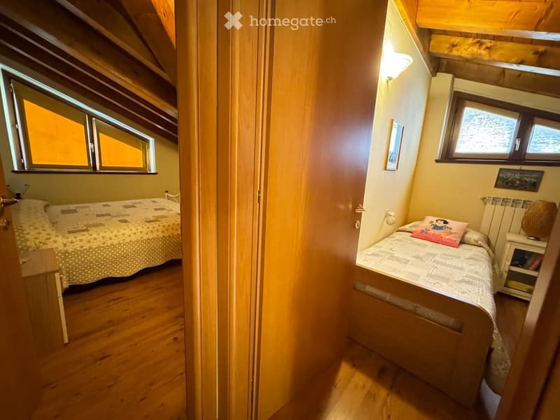 Cozy attic bedroom with wooden beams, two single beds, nightstand, and picture frame on the wall.