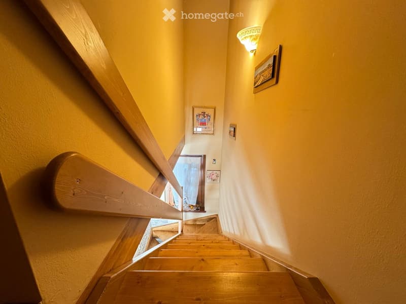 Wooden staircase with a handrail, yellow walls, framed pictures, and a wall-mounted light fixture.