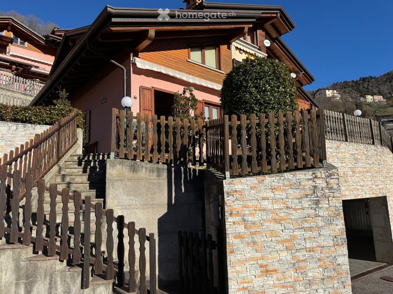 Two-story house with wooden and brick exterior, raised ground floor, wooden staircase, and wooden fence.
