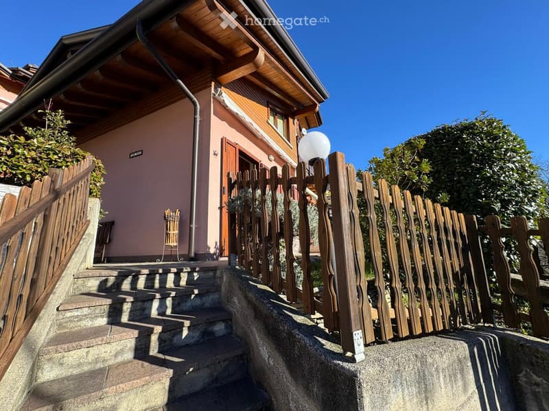 A two-story house with a wooden fence and steps leading up to the entrance, surrounded by greenery.