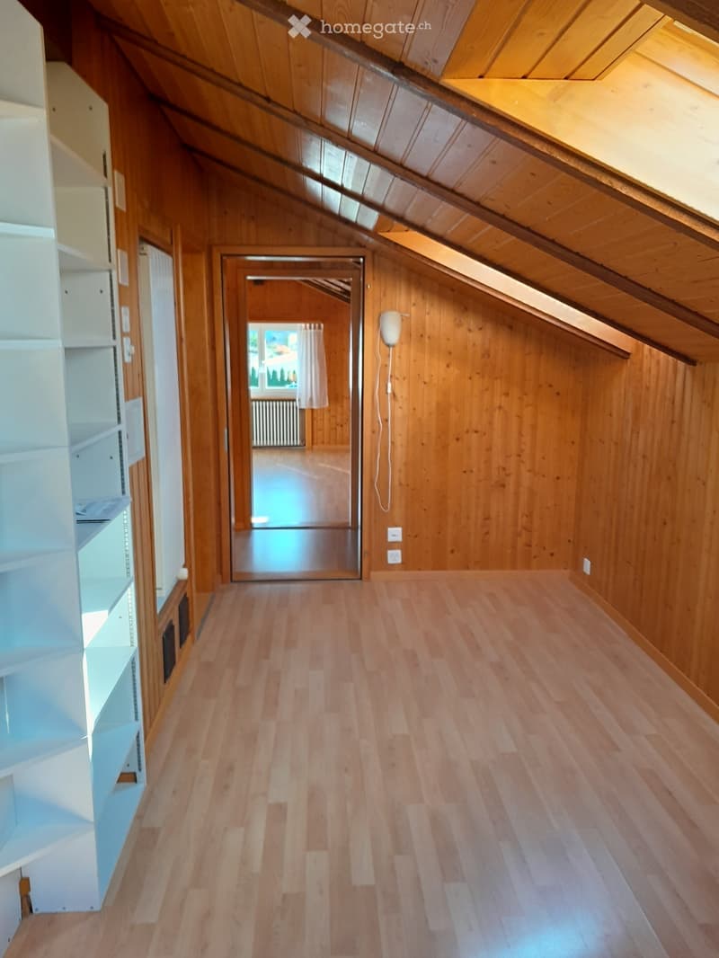 Empty hallway with wooden flooring and walls, featuring a mirror on one side and a view into another room through an open doorway.