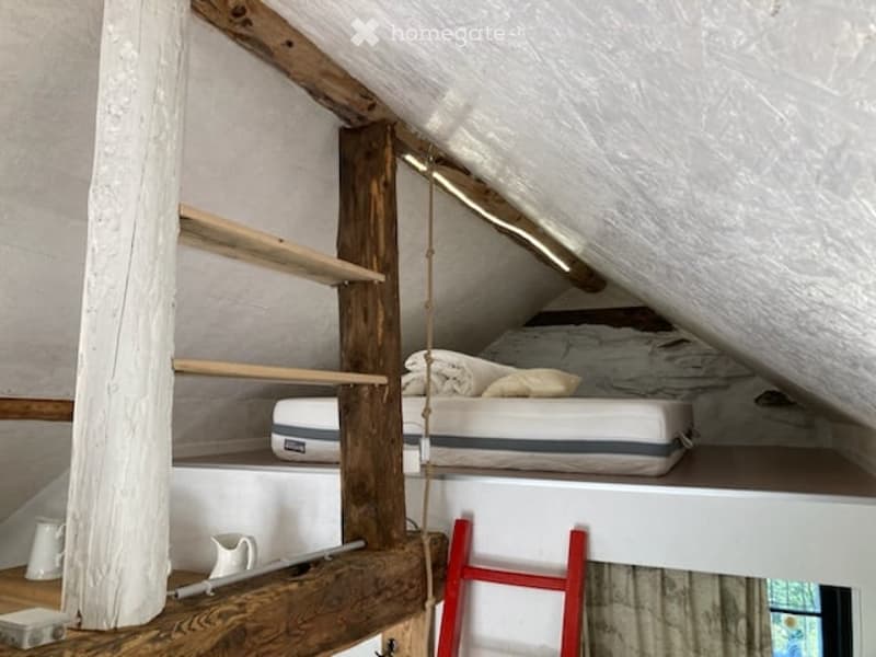 Cozy attic bedroom with a lofted bed, wooden shelves, and a small ladder leading to the sleeping platform.