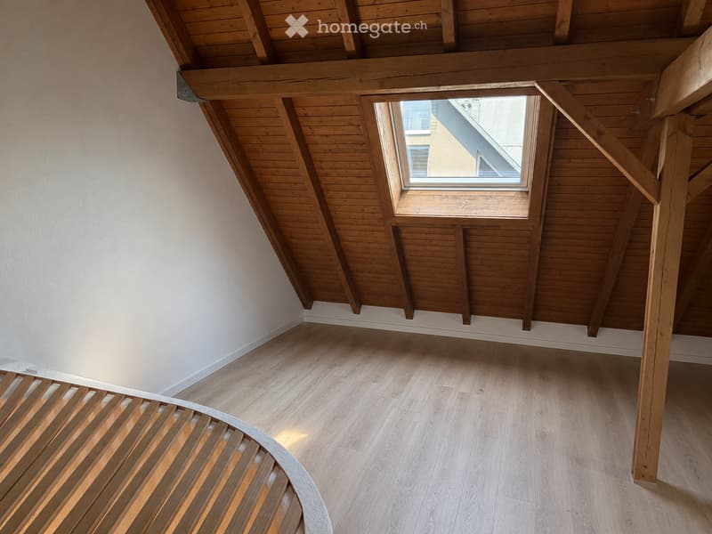 Unfurnished Room. Empty attic space with wooden beams, light wooden flooring, and a skylight window allowing natural light to enter.