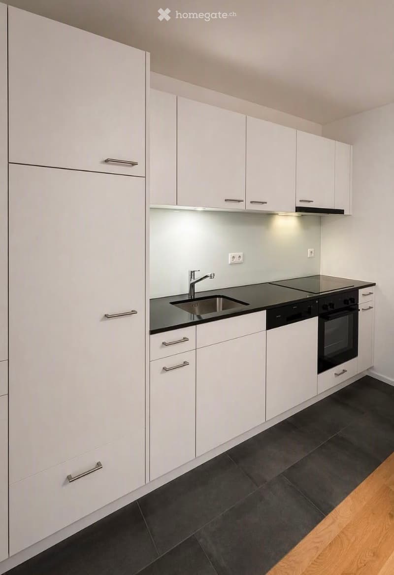 Modern kitchen with white cabinets, black countertops, stainless steel sink and faucet, built-in stove and oven, and dark tiled flooring.