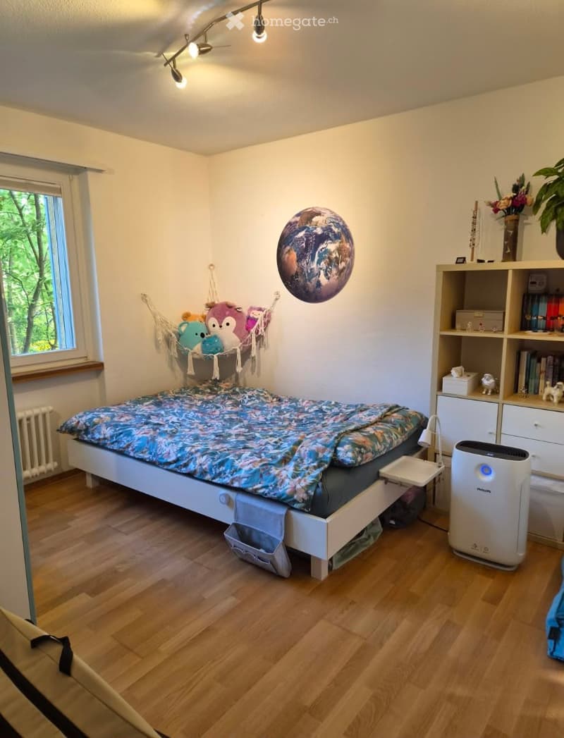 Cozy bedroom with wooden flooring, a single bed with a colorful duvet, a bookshelf filled with books and decorative items, an air purifier, a hammock with stuffed animals, and a large decorative globe on the wall.