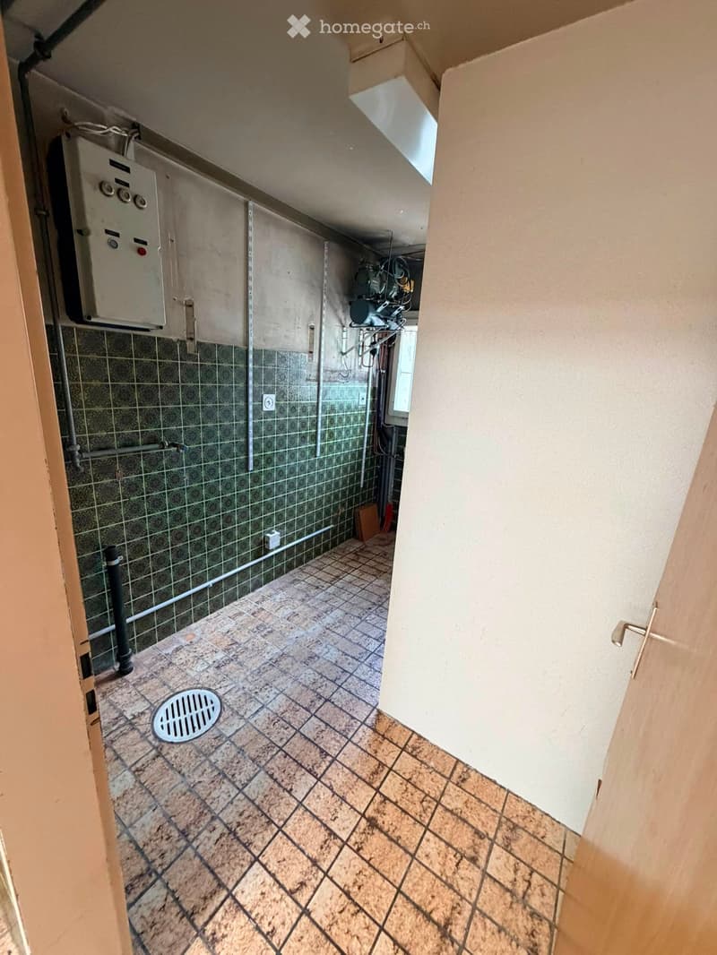 Utility area with tiled floor, green tiled wall, and various pipes and equipment.