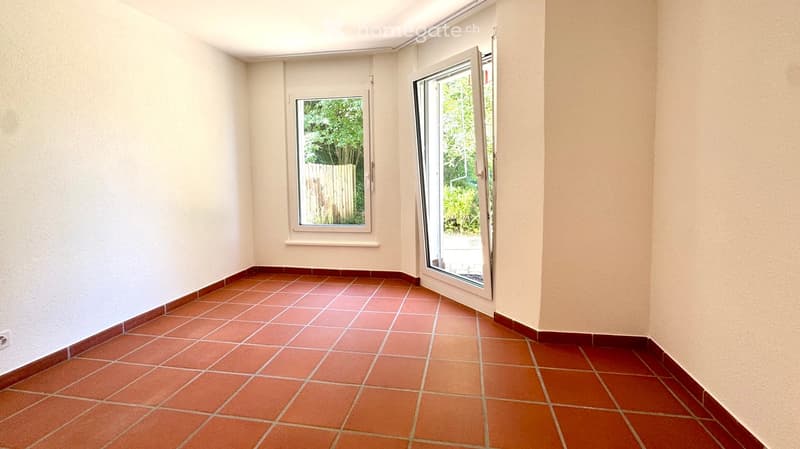 Empty room with tiled floor and white walls, featuring a large window and a sliding glass door leading outside.
