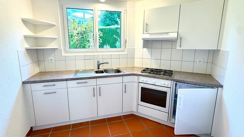 Modern kitchen with white cabinets, granite countertops, gas stove, sink, and built-in oven. Features a window with a view of greenery.