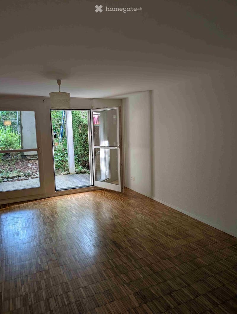 Empty room with wooden flooring, large windows, and an open sliding door leading to an outdoor area.