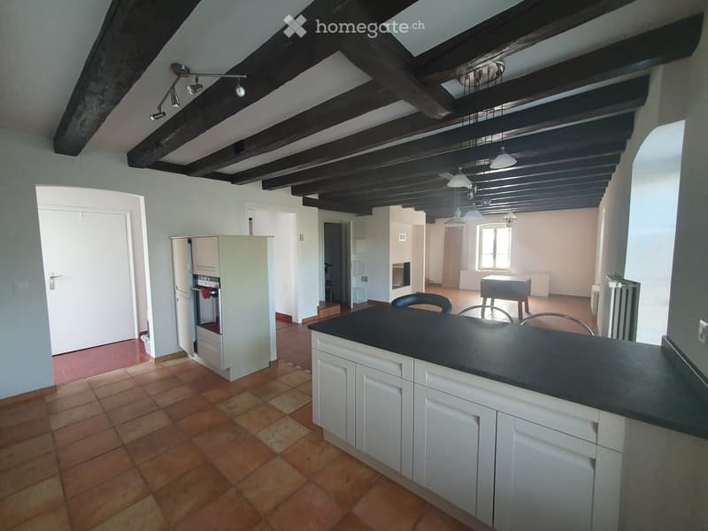 Open-plan kitchen with exposed wooden beams, tiled floor, white cabinets, black countertop, and a small dining area with a table and chairs.