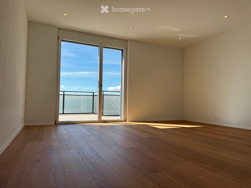 Empty room with wooden flooring, large sliding glass doors leading to a balcony with a view of the ocean.