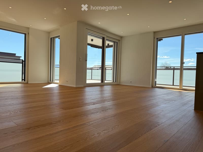 Empty room with wooden flooring, large glass sliding doors leading to a balcony, and recessed ceiling lighting.