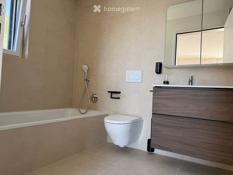 Modern bathroom with beige tiles, a bathtub, toilet, sink with wooden cabinet, and a large mirror above the sink.