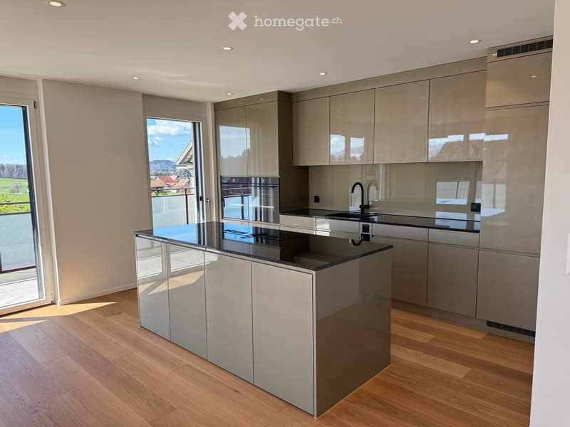 Modern kitchen with grey cabinets, a central island, and a black countertop. Features a sink, faucet, and an oven, with large windows offering a scenic view.