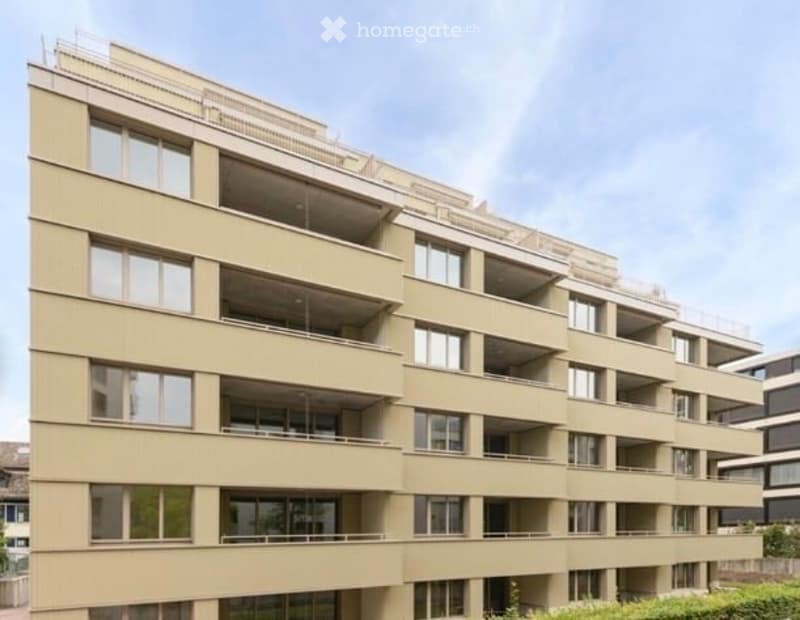 Modern multi-story residential building with beige facade, large windows, and multiple balconies.