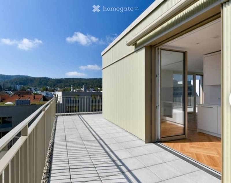 Balcony with tiled floor, metal railing, and sliding glass door leading to a room with wooden flooring and white cabinets.