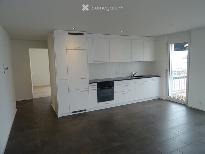 Modern kitchen with white cabinets, dark countertops, and a built-in oven. Features a dark tiled floor and a large window with a view.