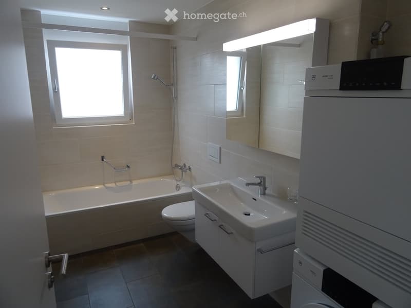 Modern bathroom with a bathtub, toilet, sink, mirror, and showerhead. Features a large window and built-in storage cabinets.