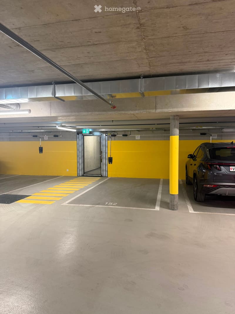 Underground parking area with concrete floors, yellow pillars, and a parked car. Features include marked parking spaces and an emergency exit.
