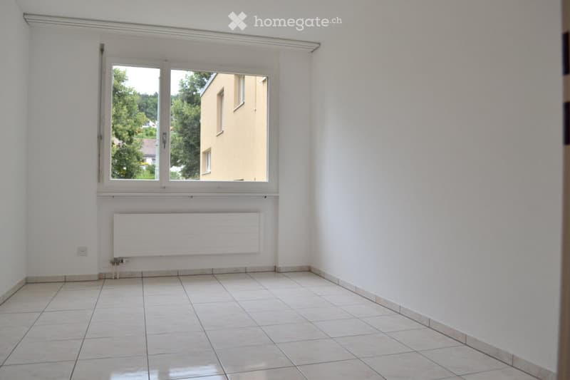 Empty room with tiled floor, white walls, large window, radiator, and visible electrical outlet.